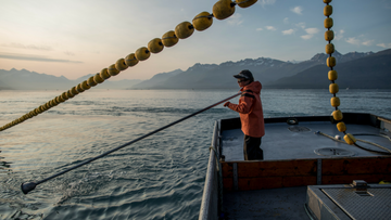 Fisherman on boat with mountains in background 